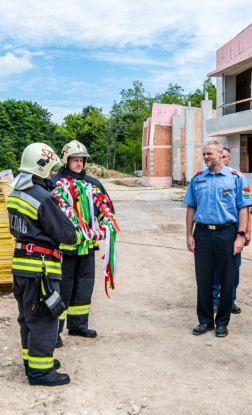 Két tűzoltó kolléga tartja a bokréta koszorút az épület előtt
