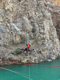 A képen a dolomit helyfal, előtte a kötélpályán, a víz fölött függeszkedő versenyző