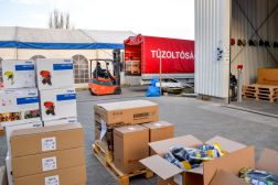 A kép előterében pakolásra kész dobozok, a háttérben egy villástargonca rakodja fel a felszereléseket egy teherautóra