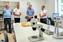 Az intézet vezetője ismerteti  vendégeknek az optikai laboratórium mérőeszközeit. Az előtérben egy Olympus S61 optikai sztereomikroszkóp látható.