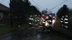 Alkonyati felvétel az útra borult fát eltávolító tűzoltókról. A képen intenzíven látható a védőruhák fényvisszaverő csíkja.