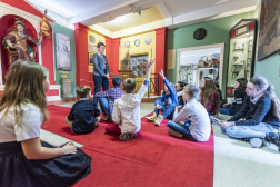 Játékos tárlatvezetés - a gyerekek a kiállítóterem szőnyegén ülve kvízkérdésekre válaszolnak