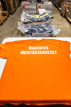 Önkéntes mentőszervezet feliratú narancssárga pólója.